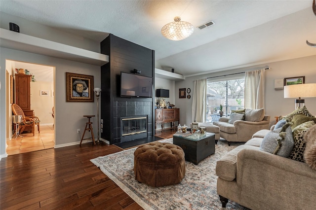 living area featuring visible vents, baseboards, lofted ceiling, a fireplace, and wood-type flooring