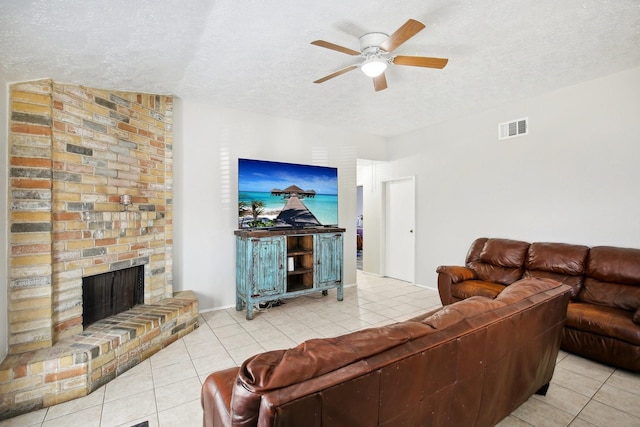 living area featuring a ceiling fan, visible vents, a fireplace, tile patterned flooring, and a textured ceiling