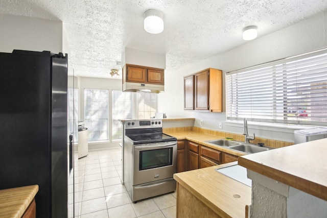 kitchen featuring light tile patterned floors, stainless steel electric stove, freestanding refrigerator, a sink, and under cabinet range hood