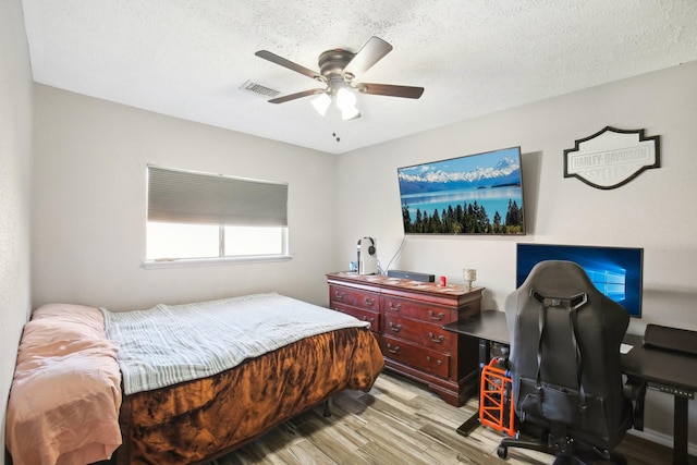 bedroom with light wood finished floors, visible vents, a textured ceiling, and ceiling fan