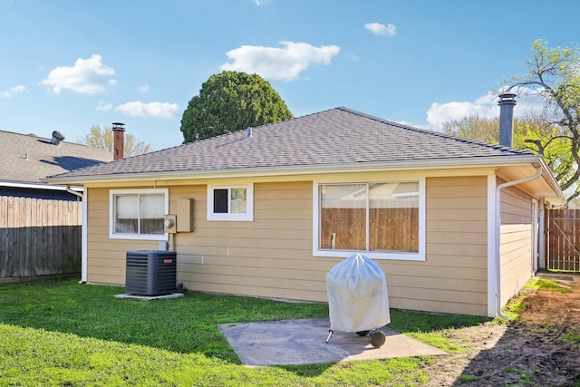 rear view of house with cooling unit, a lawn, a shingled roof, and fence