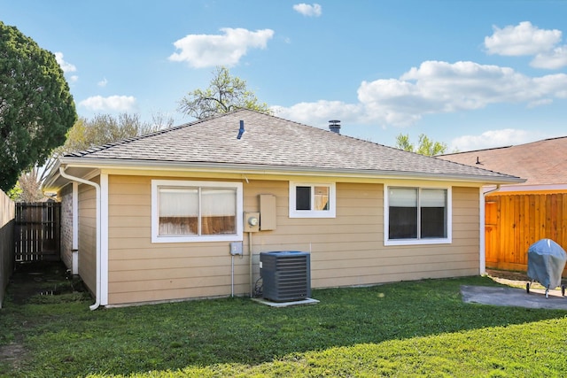 back of house with a yard, roof with shingles, central AC unit, and a fenced backyard