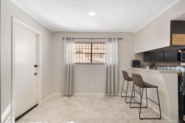 kitchen featuring baseboards, crown molding, a textured ceiling, a kitchen bar, and stainless steel microwave