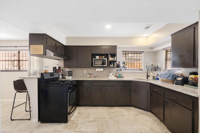 kitchen featuring stainless steel microwave, range with gas cooktop, dark brown cabinetry, under cabinet range hood, and a sink