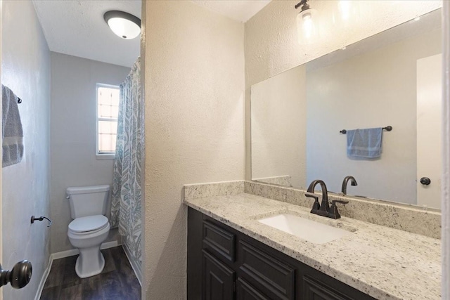 full bath with toilet, wood finished floors, baseboards, vanity, and a textured wall