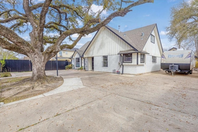 exterior space featuring brick siding, a shingled roof, concrete driveway, and fence