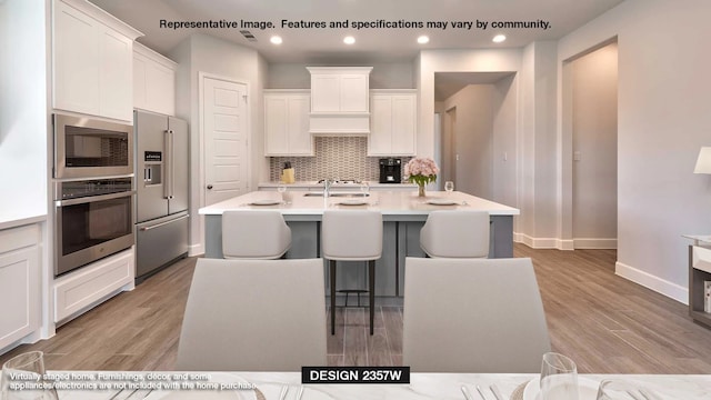 kitchen with backsplash, a kitchen bar, light countertops, appliances with stainless steel finishes, and white cabinets