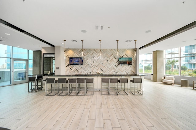 kitchen featuring hanging light fixtures, light wood-type flooring, backsplash, and a breakfast bar