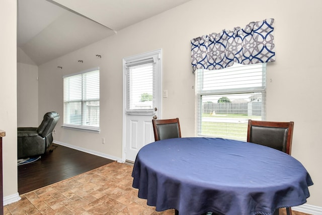 dining space featuring stone finish floor, baseboards, and vaulted ceiling