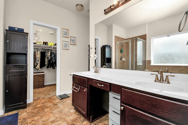 bathroom featuring a walk in closet, double vanity, a stall shower, and a sink