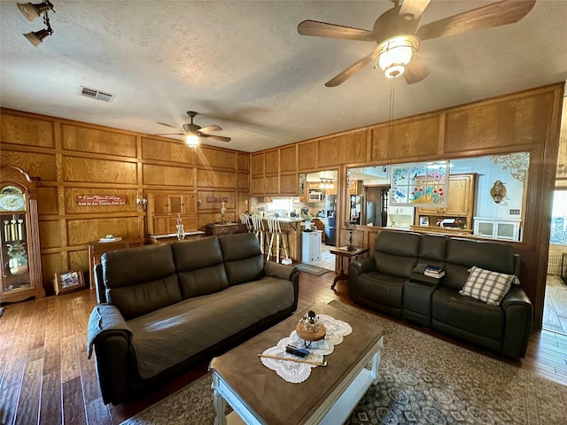 living area featuring visible vents, a ceiling fan, a textured ceiling, hardwood / wood-style floors, and wood walls