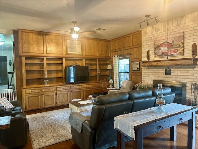 living room featuring visible vents, a ceiling fan, a textured ceiling, wood finished floors, and a brick fireplace