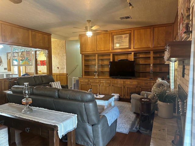 living area with visible vents, built in shelves, ceiling fan, a fireplace, and a textured ceiling