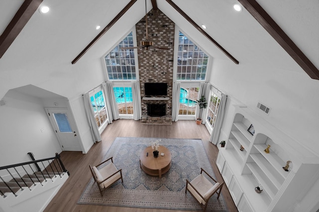 living area featuring wood finished floors, beamed ceiling, visible vents, high vaulted ceiling, and a brick fireplace