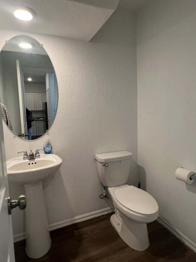 bathroom featuring toilet, wood finished floors, baseboards, and a sink