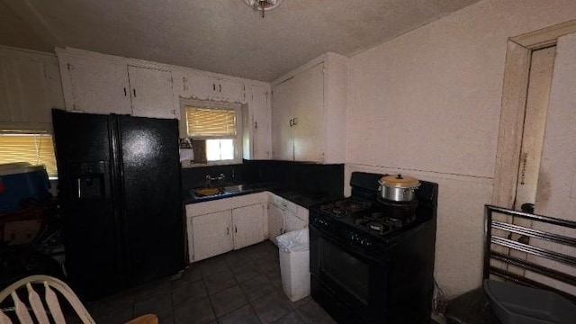 kitchen featuring dark tile patterned floors, white cabinetry, black appliances, and a sink