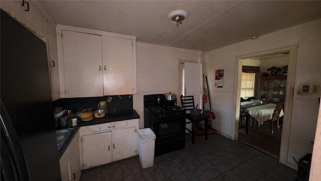 kitchen featuring black gas range, dark countertops, dark tile patterned floors, and white cabinetry