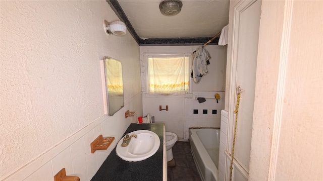 bathroom with toilet, a textured wall, a wainscoted wall, and a sink