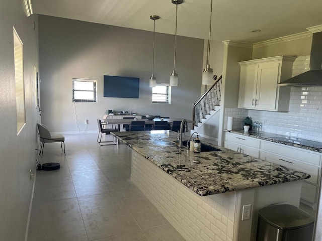 kitchen with black electric stovetop, light stone counters, decorative backsplash, white cabinets, and a sink