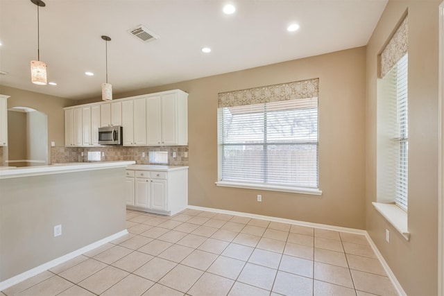 kitchen with visible vents, arched walkways, light countertops, stainless steel microwave, and backsplash