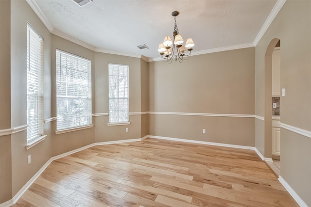 empty room with baseboards, visible vents, light wood finished floors, arched walkways, and ornamental molding