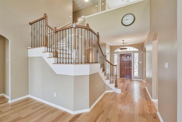 entryway with stairway, wood finished floors, baseboards, a high ceiling, and arched walkways