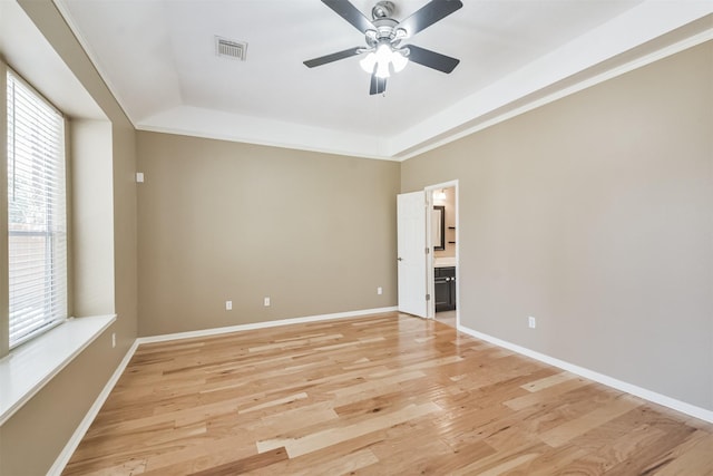 empty room with a ceiling fan, baseboards, visible vents, light wood finished floors, and a raised ceiling