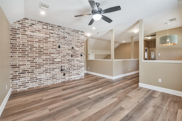 empty room featuring visible vents, wood finished floors, baseboards, brick wall, and lofted ceiling