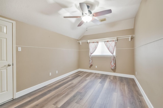 empty room with a ceiling fan, vaulted ceiling, wood finished floors, and baseboards