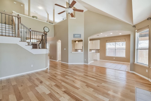 unfurnished living room with stairway, light wood-style flooring, arched walkways, and ceiling fan