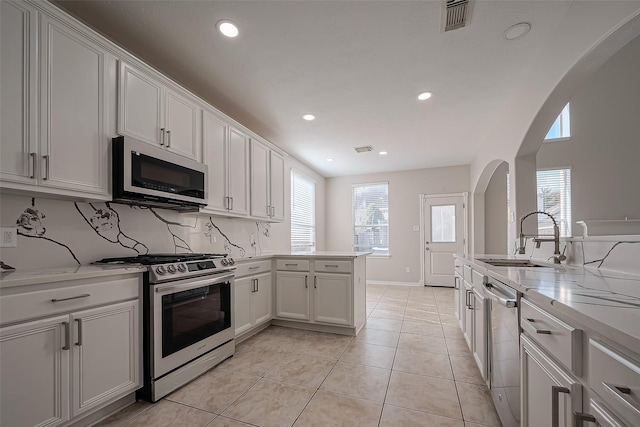 kitchen featuring a sink, backsplash, arched walkways, appliances with stainless steel finishes, and a peninsula