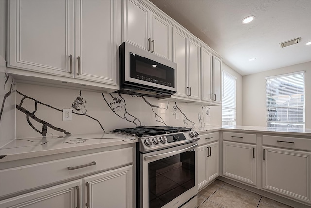 kitchen with light tile patterned floors, visible vents, stainless steel appliances, white cabinets, and tasteful backsplash