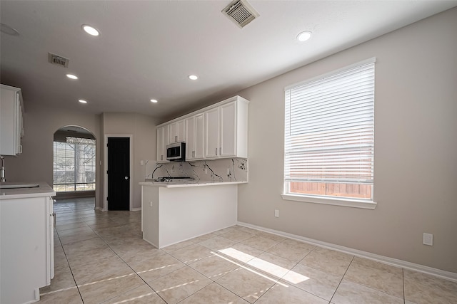 kitchen with stainless steel microwave, visible vents, arched walkways, white cabinets, and a sink