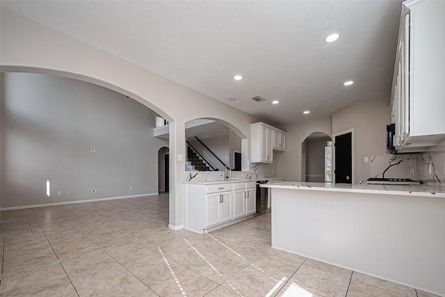 kitchen featuring tasteful backsplash, arched walkways, a peninsula, white cabinets, and light countertops