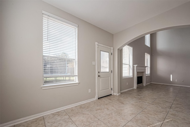 foyer entrance with light tile patterned floors, a fireplace, baseboards, and arched walkways