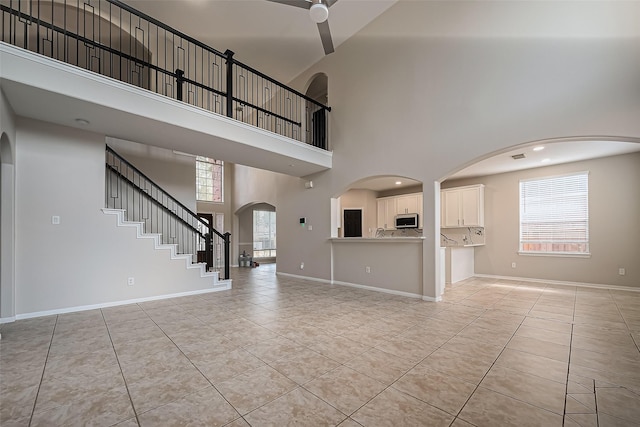 unfurnished living room with light tile patterned floors, a ceiling fan, a high ceiling, and baseboards