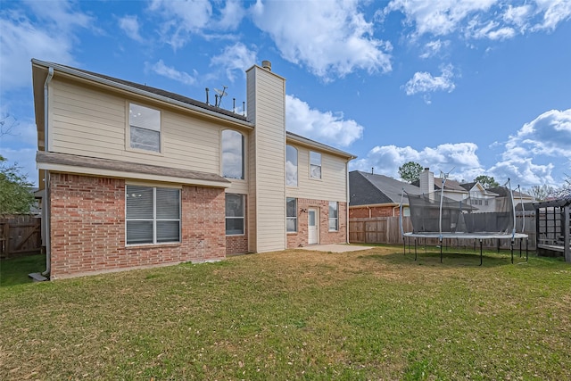 back of property featuring a yard, a fenced backyard, a trampoline, a patio area, and brick siding