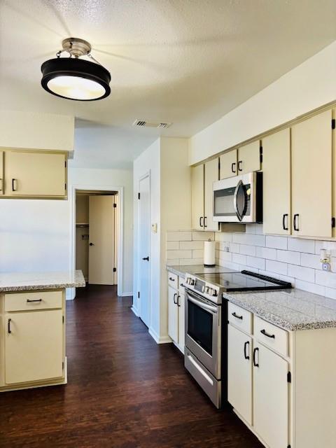 kitchen featuring dark wood finished floors, decorative backsplash, appliances with stainless steel finishes, and visible vents