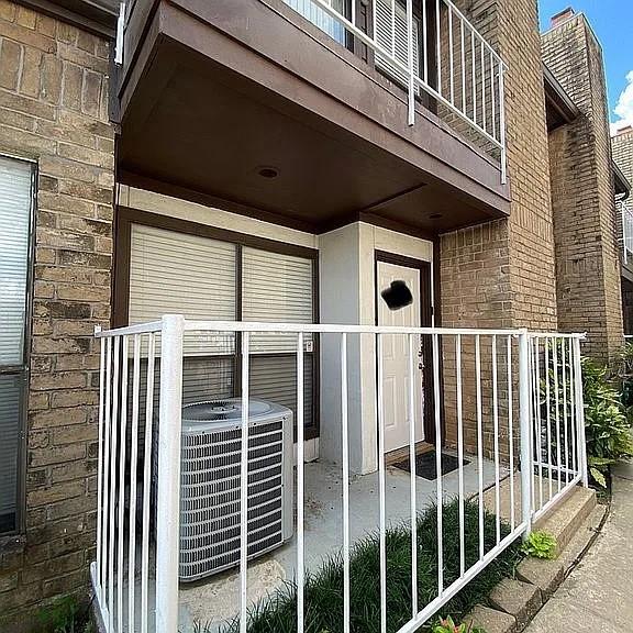 view of exterior entry featuring brick siding, central AC, and a balcony