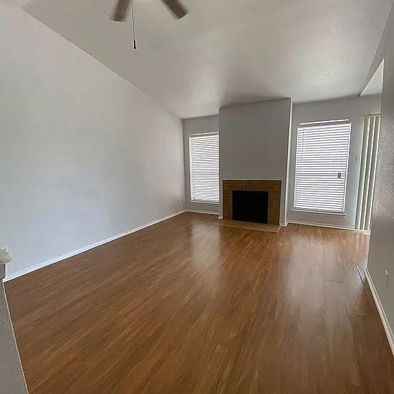 unfurnished living room with a fireplace, a ceiling fan, baseboards, and wood finished floors