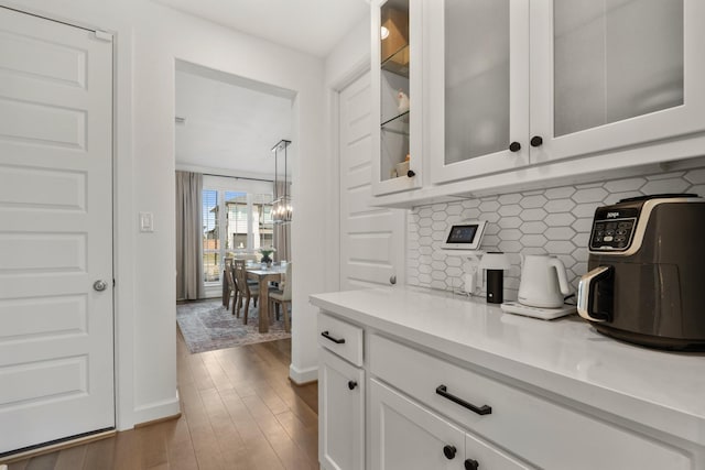 bar with baseboards, backsplash, an inviting chandelier, and wood finished floors