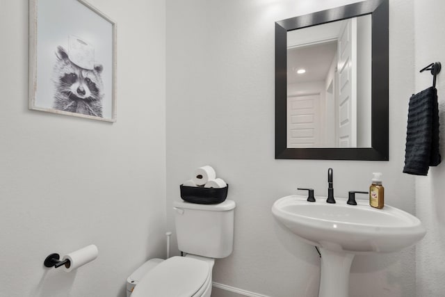 half bath featuring toilet, baseboards, and a sink