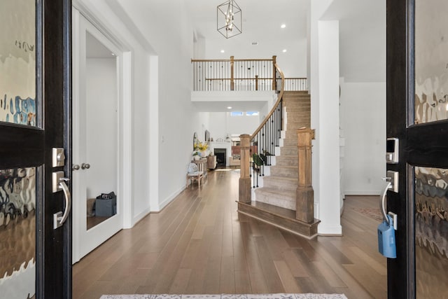 foyer entrance with stairway, recessed lighting, a fireplace, a towering ceiling, and wood finished floors