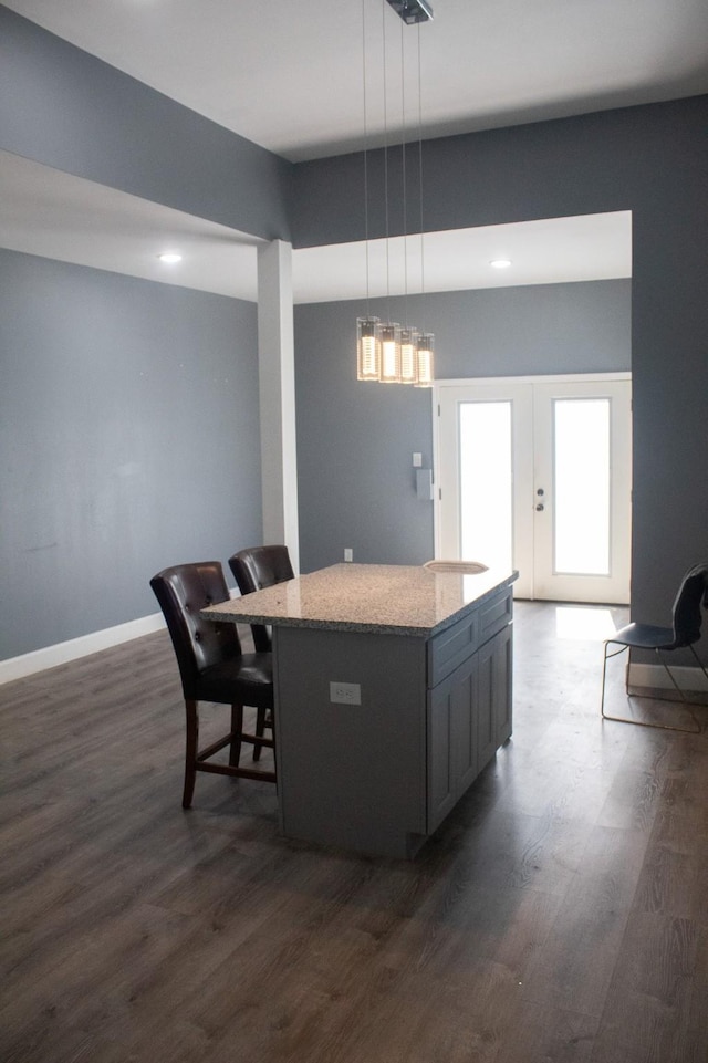 kitchen featuring a center island, dark wood-type flooring, baseboards, pendant lighting, and light stone counters