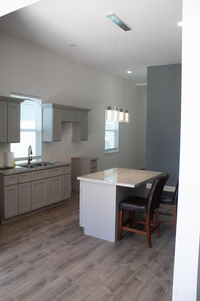 kitchen featuring a kitchen island, light stone countertops, gray cabinets, wood finished floors, and a sink