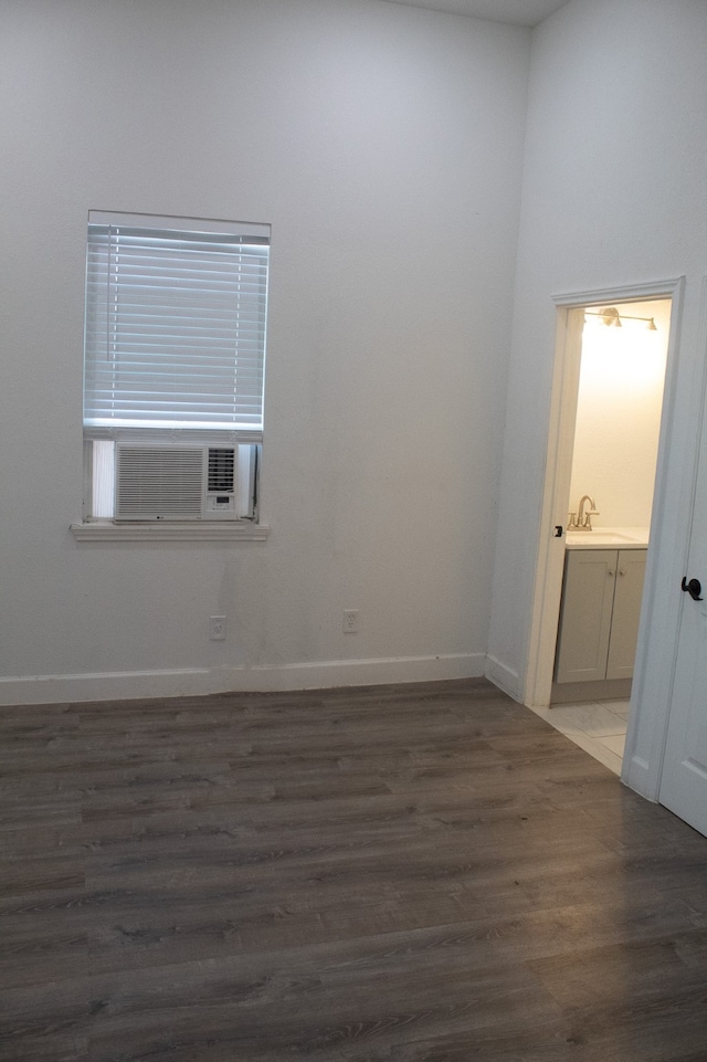 unfurnished room with a sink, cooling unit, baseboards, and wood finished floors