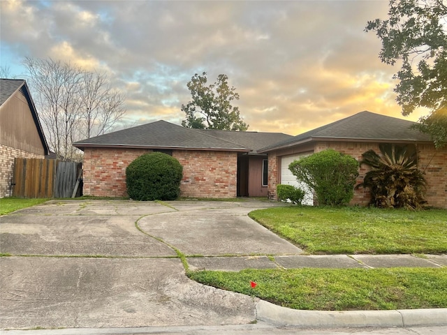 ranch-style home featuring brick siding, fence, driveway, a yard, and an attached garage