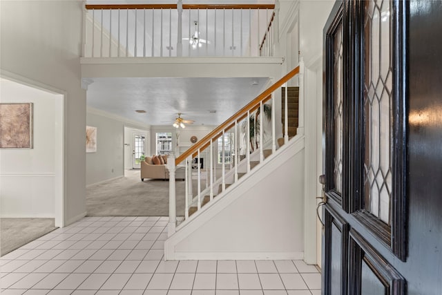 foyer featuring stairway, light tile patterned floors, baseboards, light colored carpet, and ceiling fan