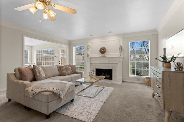 living area featuring baseboards, ceiling fan, a tiled fireplace, crown molding, and light colored carpet