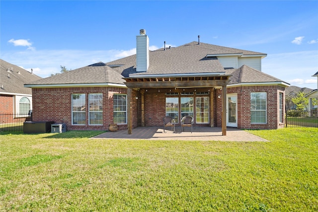 back of house with brick siding, a shingled roof, fence, a lawn, and a patio